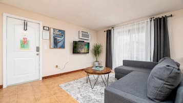 A living room with a grey sofa, a coffee table, a TV, and a door with a bulletin board.