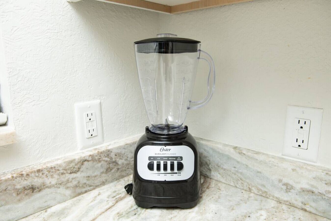 A blender on a kitchen counter with a white wall and marble backsplash.