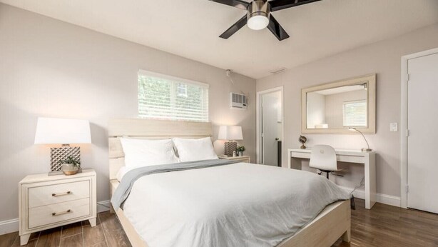 A bedroom with a bed, bedside tables, a desk, a chair, a ceiling fan, and a window.