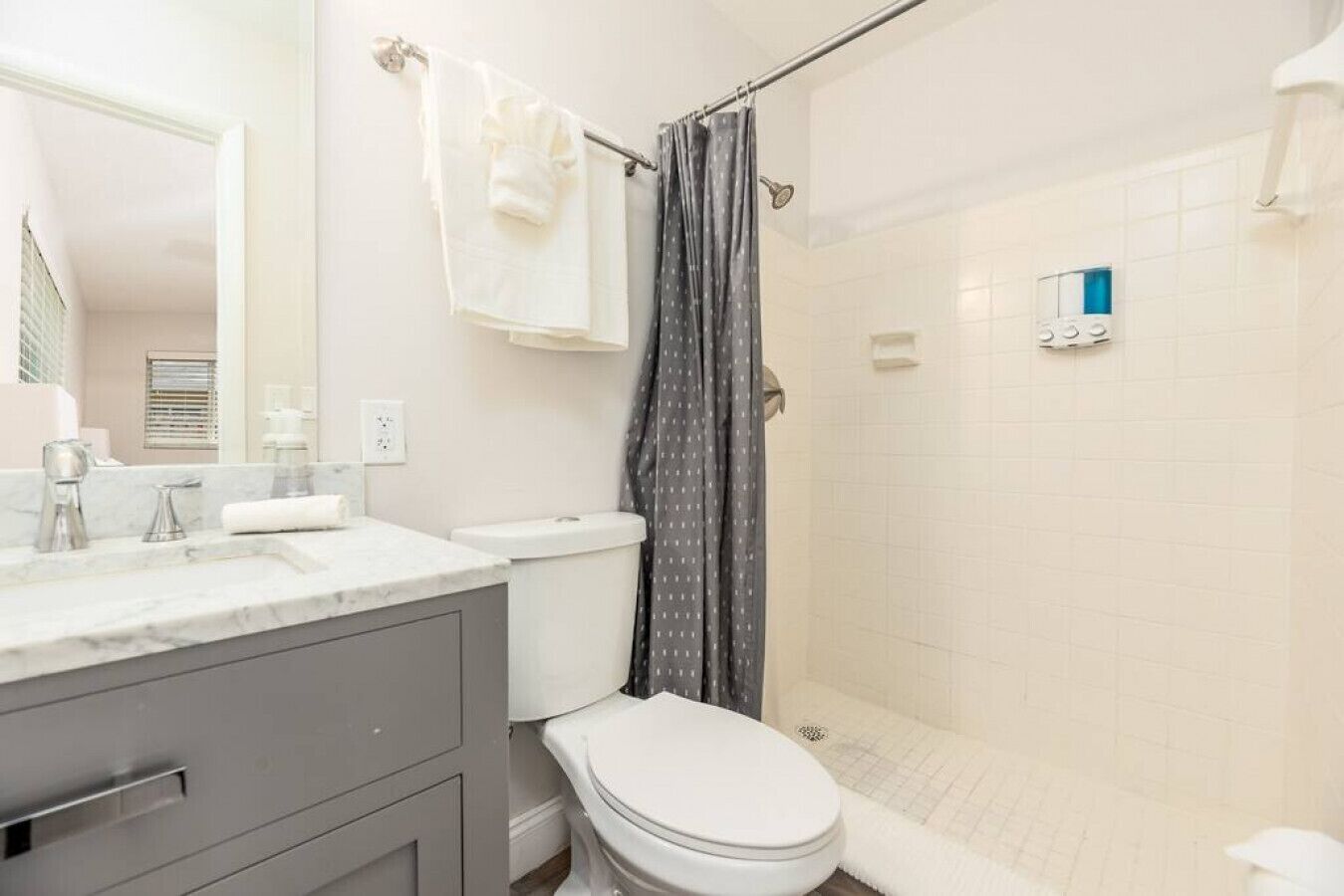 A bathroom with a white toilet, a shower with a grey curtain, a marble sink, and a mirror.