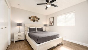 A bedroom with a bed, nightstands, a ceiling fan, a window with blinds, and a wall art piece. - The Guesthouse #4 - Wilton Manors (Wilton Manors)