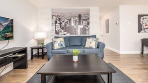 A modern living room with a blue sofa, a coffee table, a cityscape painting, and a television. - The Guesthouse #4 - Wilton Manors (Wilton Manors)