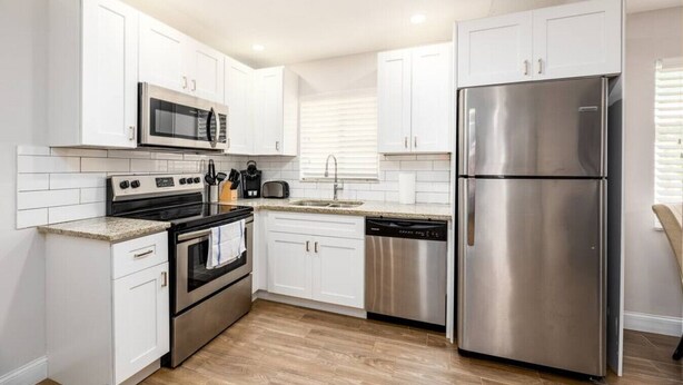 A modern kitchen with white cabinets, stainless steel appliances, and a wooden floor. - The Guesthouse #4 - Wilton Manors (Wilton Manors)