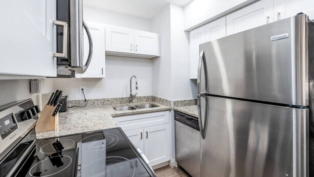 Una cocina moderna con electrodomésticos de acero inoxidable, armarios blancos y encimeras de granito.
