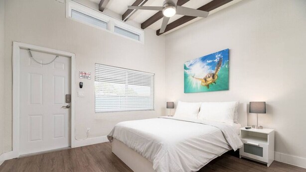 A bedroom with a bed, a nightstand, a wall-mounted painting, a door, and a window with blinds. - The Hideaway at Lake Ridge #2 (Fort Lauderdale)
