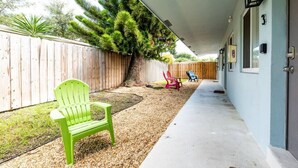Une terrasse extérieure couverte, dotée d’un sol en béton, d’une clôture en bois et d’un grand arbre. On y trouve deux chaises et une petite table.