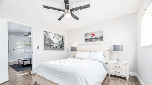 Une chambre à coucher comprenant un lit, des tables de chevet, un ventilateur de plafond et des œuvres d’art accrochées aux murs.