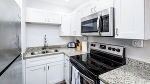 Une cuisine moderne avec des armoires blanches, un réfrigérateur en acier inoxydable, un four à micro-ondes, une cuisinière électrique et un comptoir en granit.