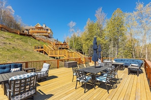 A wooden deck with outdoor furniture and a staircase leading to a building. - Luxury Torch Lake Vacation Home – Private Dock, Pickleball, Game Room, Theatre (Kewadin)