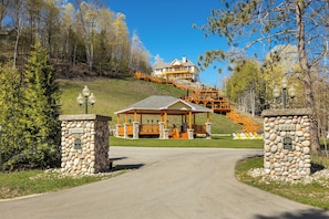 A lodge with a stone entrance, a gazebo, and a staircase leading to a house. - Luxury Torch Lake Vacation Home – Private Dock, Pickleball, Game Room, Theatre (Kewadin)