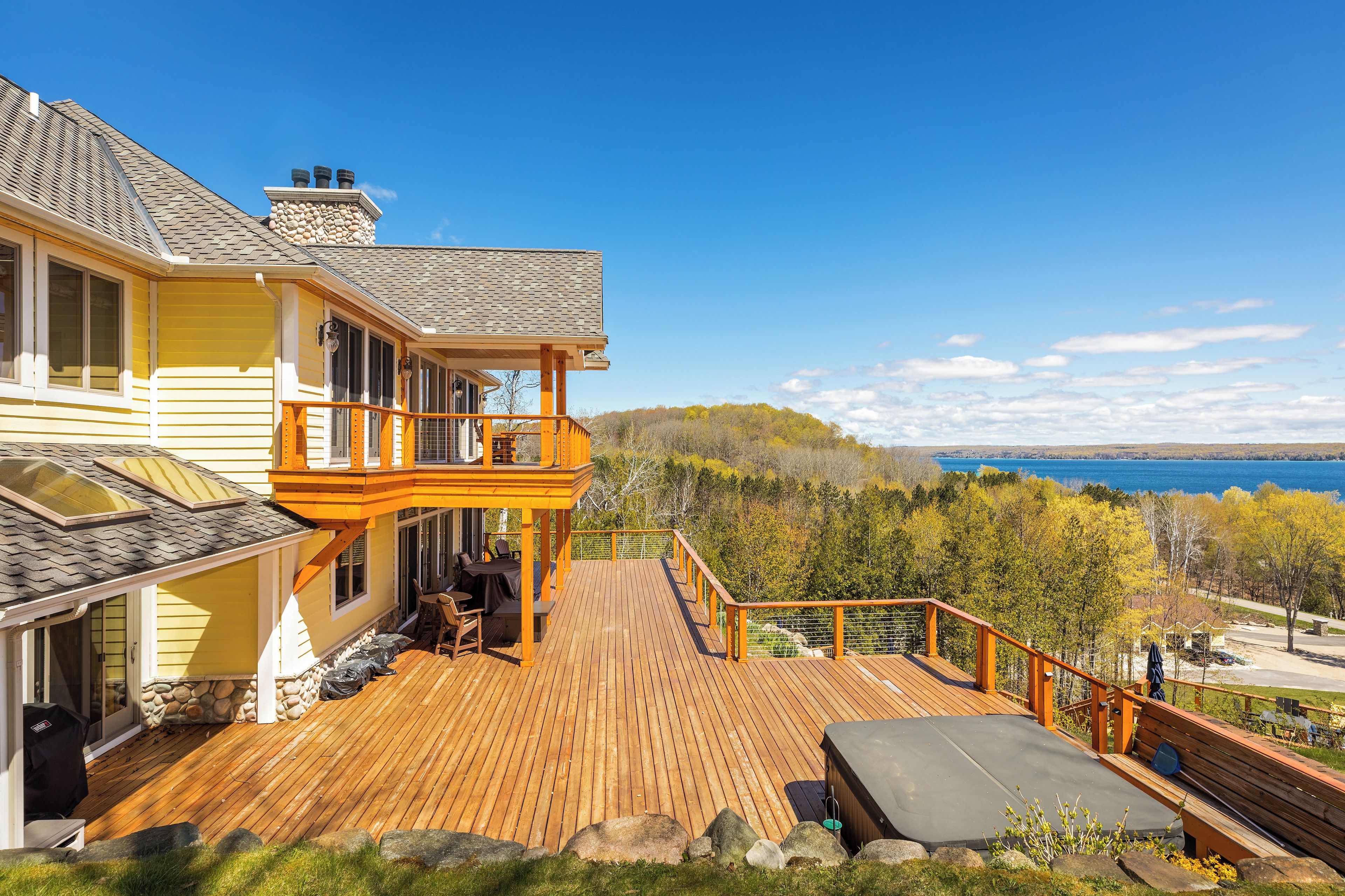 A two-story house with a deck, a stone fireplace, and a view of a lake.