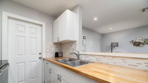A modern kitchen with white cabinetry, a wooden countertop, and a stainless steel sink. - The Palms @ Middle River Terrace #3 (Fort Lauderdale)