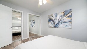 A bedroom with a bed, a ceiling fan, a large abstract painting, and a glass door leading to another room. - The Palms @ Middle River Terrace #3 (Fort Lauderdale)