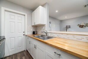 A modern kitchen with white cabinetry, a wooden countertop, a double sink, and a backsplash with a mosaic tile pattern.