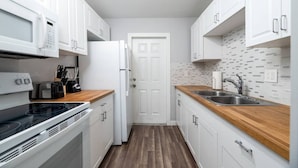 A compact kitchen with white cabinets, a microwave, a toaster, a refrigerator, and a wooden countertop.
