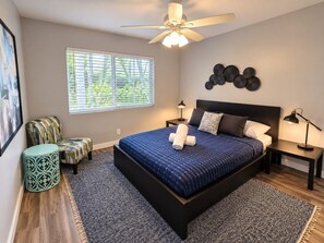 A bedroom with a bed, a ceiling fan, a window with blinds, a wall art piece, and a side table with a lamp. - The Palms @ Middle River Terrace #2 (Fort Lauderdale)