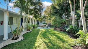 A courtyard with palm trees, a small garden, and a building with a white exterior and blue doors.