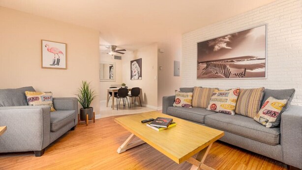 Uma sala de estar moderna com um sofá cinzento, uma mesa de centro de madeira e um espaço de jantar com mesa e cadeiras.