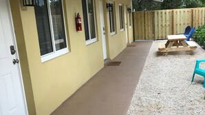 Uma área externa coberta com um caminho de concreto, uma mesa de madeira e duas cadeiras.