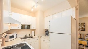 Cozinha compacta com armários brancos, micro-ondas, fogão, pia e geladeira.