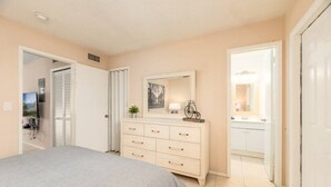 Um quarto com uma cama, cômoda, espelho e porta de acesso a um banheiro.