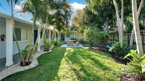 A courtyard with palm trees, a small garden, and a building with a white exterior and blue doors.