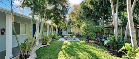 Um pátio com palmeiras, um pequeno jardim e um edifício com fachada branca e portas azuis.