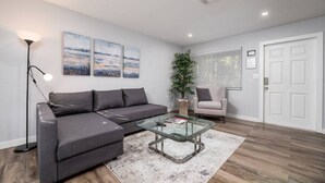 Een moderne woonkamer met een grijze modulaire bank, een glazen salontafel, een vloerlamp en een pot met een plant.