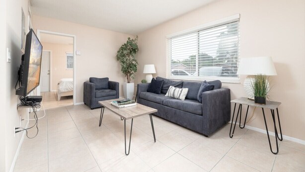 A modern living room with a grey sofa, a coffee table, a TV, and a window with blinds. - The Retreat #1 - Wilton Manors (Wilton Manors)