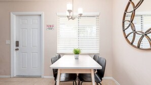 A dining area with a white table, black chairs, a potted plant, a chandelier, and a decorative wall piece. - The Retreat #1 - Wilton Manors (Wilton Manors)
