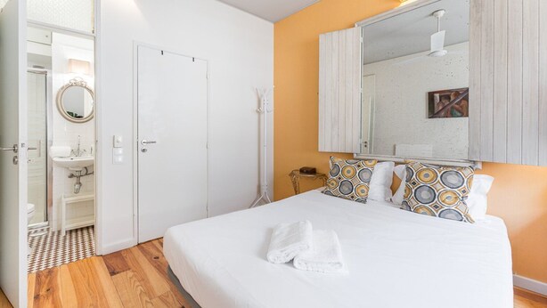Une chambre avec un grand lit, du linge de lit blanc, un miroir au-dessus du lit et un plancher en bois.