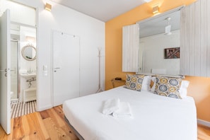 Una camera da letto con un letto grande, biancheria da letto bianca, uno specchio sopra il letto e un pavimento in legno.