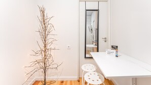 Une pièce au décor minimaliste, avec une table blanche, deux tabourets blancs, une branche décorative et un panneau d’accueil.