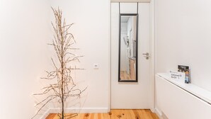 Un couloir avec une porte blanche, un miroir, une plante et une pancarte de bienvenue.