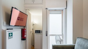 A room with a television, a fire extinguisher, a microwave, and a fan near a window.