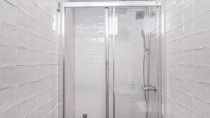 A glass-enclosed shower with a chrome showerhead and control panel, tiled walls, and a white ceiling. - GuestReady Economy - Riber Porto 4R (Porto)