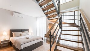 A modern bedroom with a large bed, a wooden staircase, and a desk with a chair. - GuestReady - Porto by the Bridge (Vila Nova de Gaia)