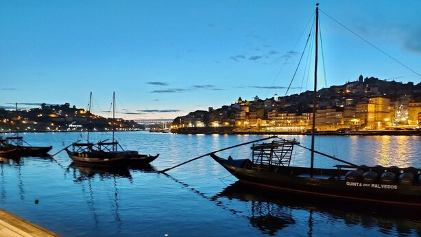 A calm waterfront with boats docked, a wooden walkway, and a cityscape with illuminated buildings in the background. - GuestReady - Porto by the Bridge (Vila Nova de Gaia)