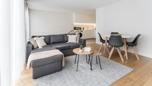 A modern living room with a grey sofa, a coffee table, and a dining area with a white table and black chairs. - GuestReady - Porto by the Bridge (Vila Nova de Gaia)