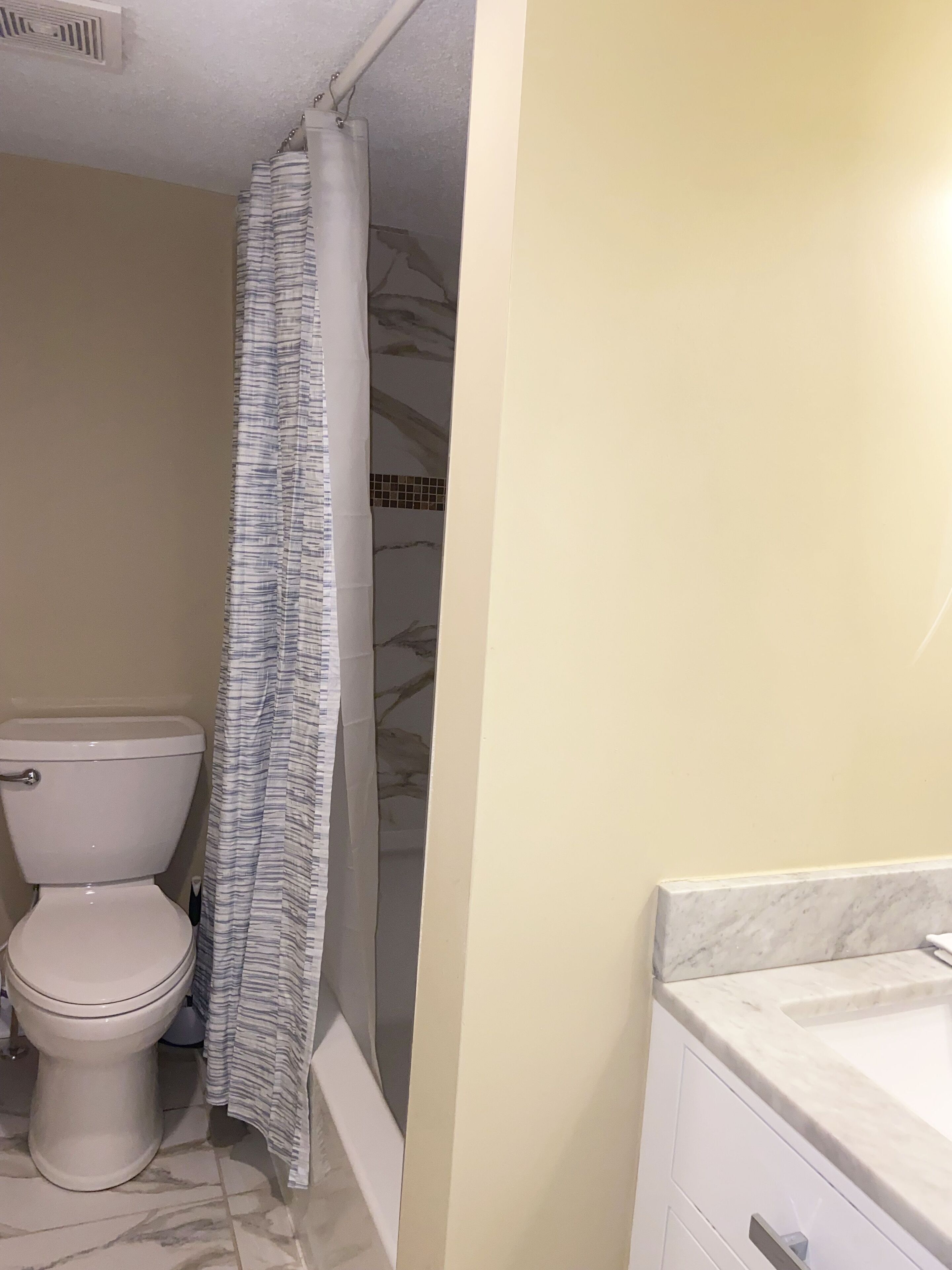 A bathroom with a toilet, a shower curtain, and a marble-tiled floor.