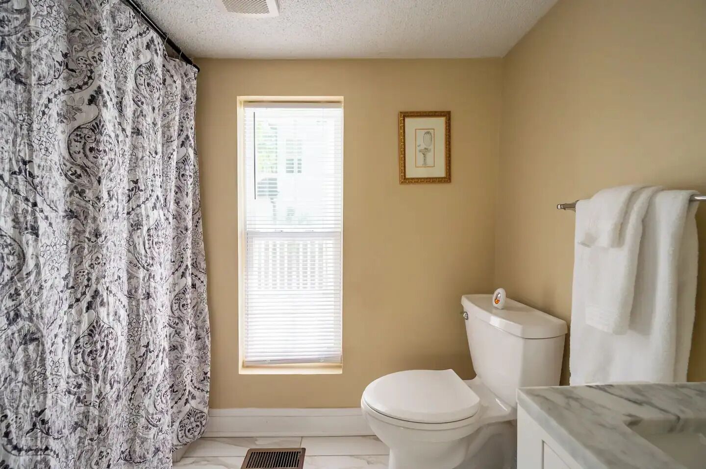 Un baño con inodoro, cortina de ducha, ventana y toallero.