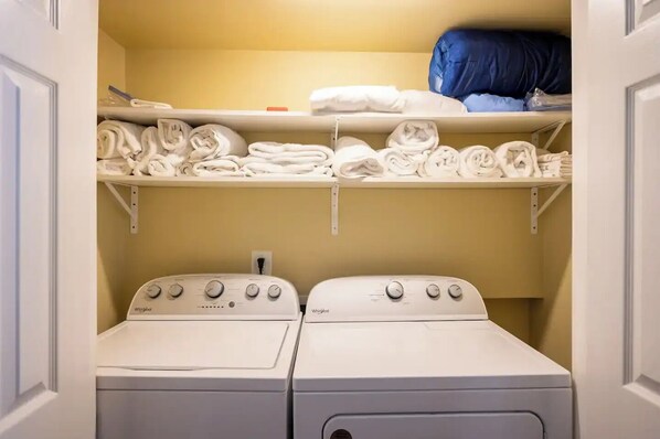 Une buanderie équipée de deux sèche-linge Whirlpool et d’une étagère au-dessus où sont pliées les serviettes.