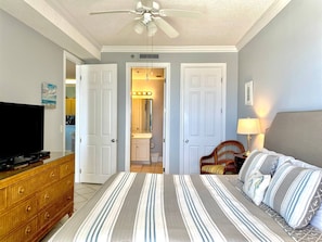 A bedroom with a bed, a TV, a dresser, a ceiling fan, and a bathroom visible through an open door. - Island Royale P103. Beachfront Penthouse living at its best with Gorgeous views! (Gulf Shores)