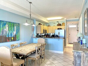 Een keuken met een centraal eiland, houten stoelen, een eettafel en een schilderij aan de muur.