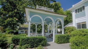 Un portico coperto con colonne bianche e tetto, immerso nel verde e con un vialetto.
