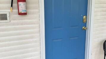 Una puerta azul con el número 2, un extintor y un felpudo.