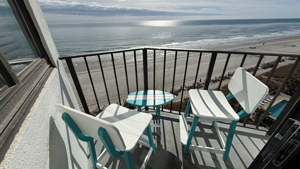 A balcony with a table and chairs overlooking a beach. - Oceanfront Studio Suite with breathtaking views (Myrtle Beach)
