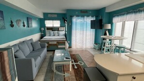 A compact, well-lit room with a bed, a sofa, a small dining table, and a kitchenette area. - Oceanfront Studio Suite with breathtaking views (Myrtle Beach)
