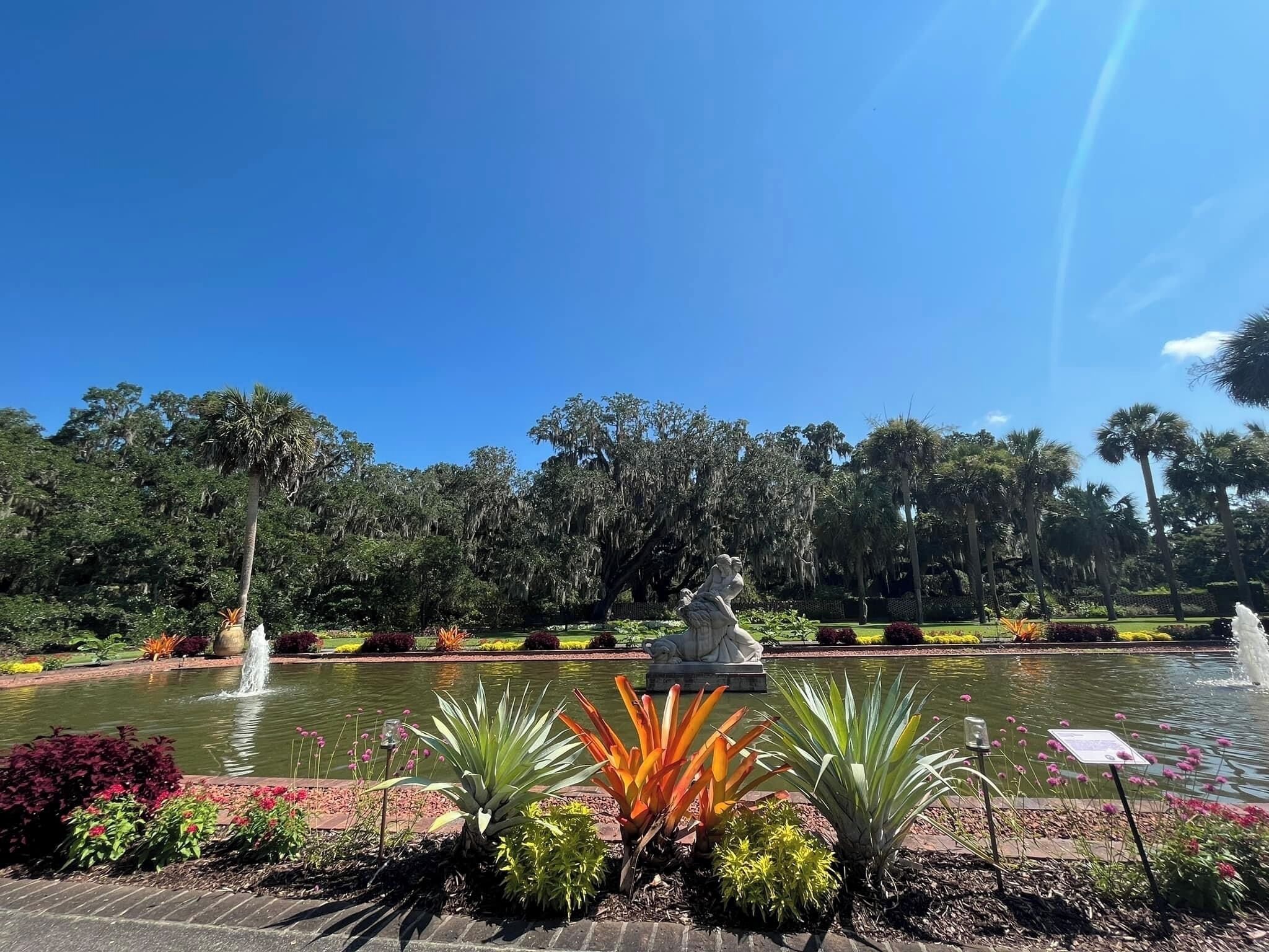 Ein friedlicher Garten mit einem zentralen Brunnen, umgeben von üppigem Grün und blühenden Pflanzen.