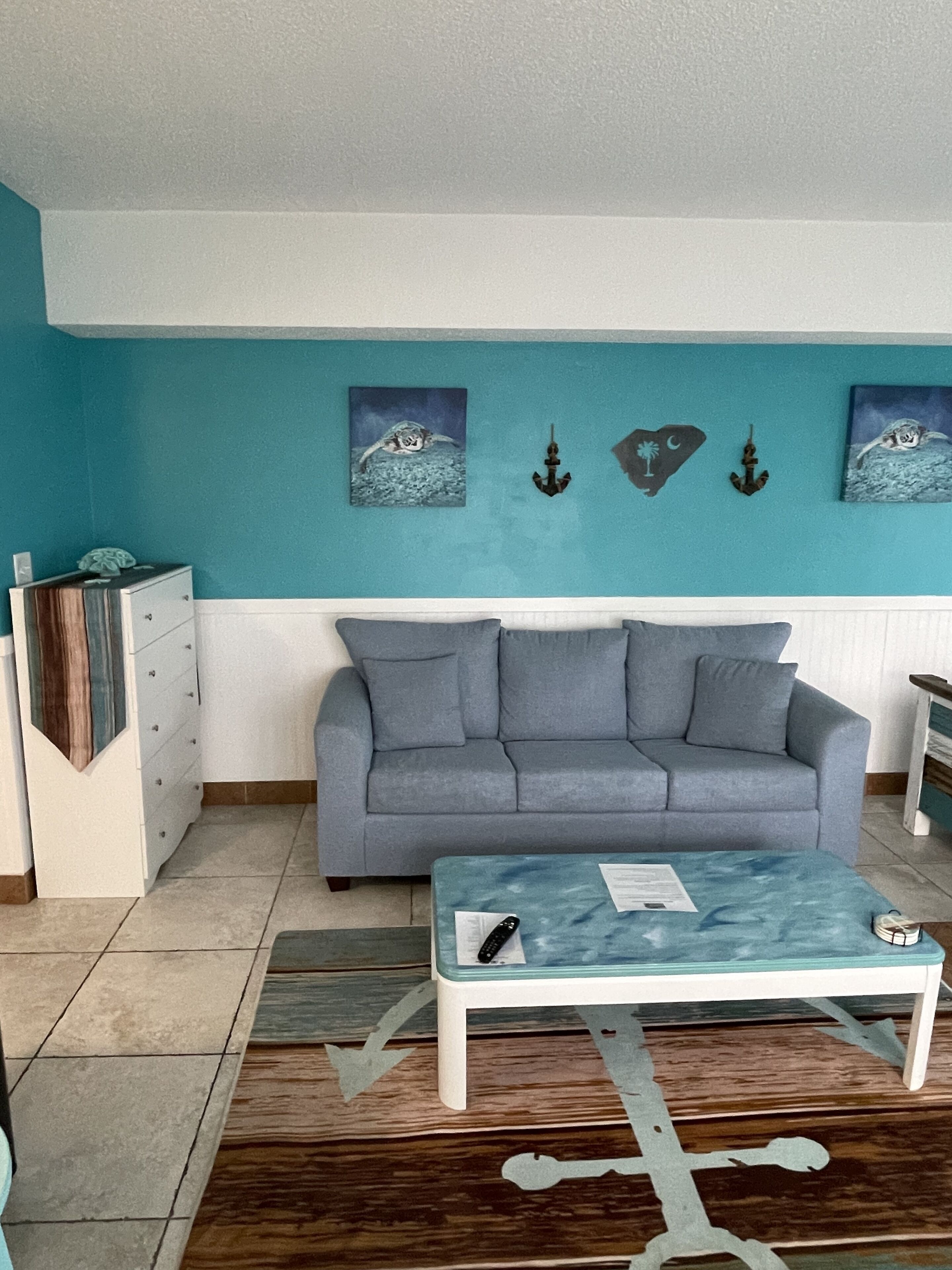 A living room with a grey sofa, a coffee table, and artwork on the walls.